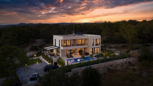 Une maison moderne à deux étages, dotée d’une piscine, entourée d’arbres et d’un paysage rocheux.