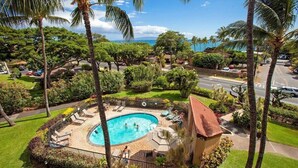 A residential area with a swimming pool surrounded by palm trees and a view of the ocean. - Oceanview Condo | Steps to Beach | Updated | A/C | Pool | Tennis (Kihei)