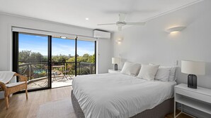 Ein modernes Schlafzimmer mit einem großen Bett, zwei Nachttischlampen, einem Deckenventilator und Blick auf einen Pool durch eine Schiebetür.
