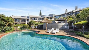 Ein Pool mit Liegestühlen, umgeben von einem angelegten Garten und einem Gebäude mit mehreren Balkonen.