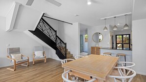 Ein modernes Interieur mit einem Holzesstisch, weißen Stühlen, einer schwarzen Treppe und Pendelleuchten.