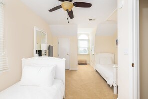 A bedroom with two beds, a ceiling fan, a window, and a door.