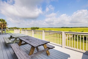 A wooden deck with picnic tables and a white railing overlooking a green field.