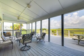A covered outdoor deck with seating and a view of a green landscape.