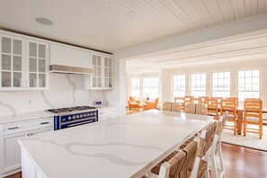 A spacious kitchen with white cabinetry, a large island, and a dining area with wooden chairs.