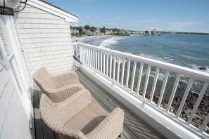 A balcony with wicker chairs overlooking a beach and ocean.