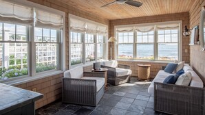A sunlit room with wicker furniture, large windows, and a ceiling fan. - Spectacular 4-Bedroom Luxury Home with Ocean and Mother's Beach Views! (Kennebunk)