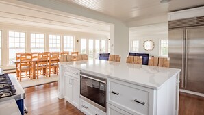 A spacious kitchen with a large island, wooden chairs, and a stainless steel refrigerator. - Spectacular 4-Bedroom Luxury Home with Ocean and Mother's Beach Views! (Kennebunk)