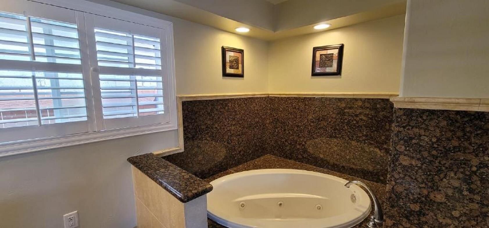 A bathroom with a freestanding bathtub, granite countertops, and a window with blinds.