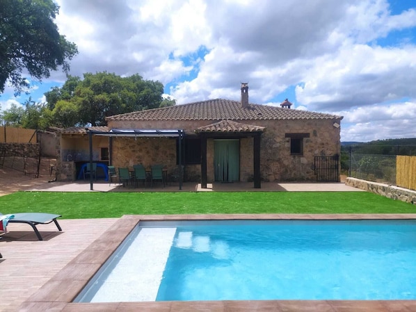 Una casa de piedra con techo de tejas, piscina y jardín con césped.