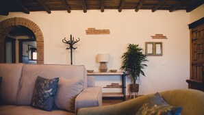 Una sala acogedora con sofá, sillón y una mesita de noche con lámpara y objetos decorativos.