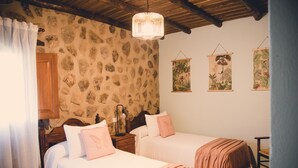 Un dormitorio con dos camas, paredes de piedra, vigas de madera y decoración botánica en la pared.