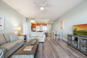 A spacious living area with a sofa, coffee table, and dining set. A kitchen is visible in the background. - Serenity of PCB @ Laketown Wharf Sleeps 8 (Panama City Beach)