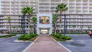 Een hotelentree met een middellange pad, palmbomen en een groot bord.
