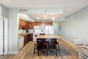 A modern kitchen with wooden cabinets, a central island with stools, a microwave, and a refrigerator. - Serenity of PCB @ Laketown Wharf Sleeps 8 (Panama City Beach)