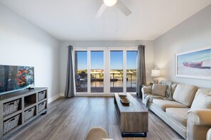 A spacious living room with a large window, a flat-screen TV, a sofa, a coffee table, and a wooden cabinet.