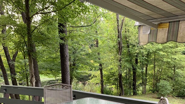 A wooden deck with a glass table and two chairs, surrounded by trees. - Peaceful Get-Away Near Conneaut Lake (Harmonsburg)