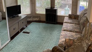 A living room with a ceiling fan, a fireplace, a sofa, a television, and a window with blinds. - Peaceful Get-Away Near Conneaut Lake (Harmonsburg)