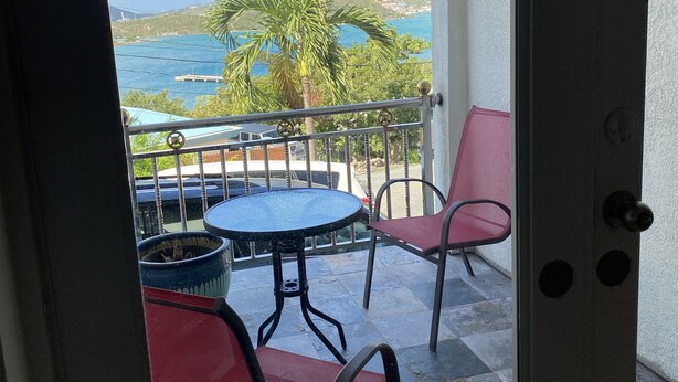 Ein Balkon mit Tisch und Stühlen, Blick auf das Meer und eine Palme.