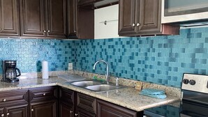 Eine Küche mit dunklen Holfschränken, einer Granit-Arbeitsplatte, einer Edelstahl-Spüle, einer eingebauten Mikrowelle und einem Backofen.