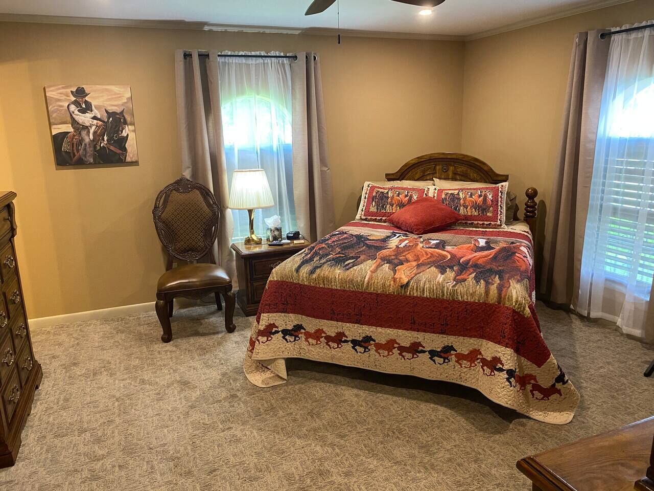 A bedroom with a large bed, a chair, a nightstand, a lamp, and a wall painting.