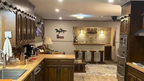 A kitchen with wooden cabinets, a central island, a bar area with stools, and a refrigerator. - StockYards!  Walk 3 Blocks-Ranch House sleeps 8, TCU close by (Ft Worth)