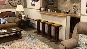 A cozy living room with a bar area, featuring a wooden bar counter, stools, and a rustic decor theme. - StockYards!  Walk 3 Blocks-Ranch House sleeps 8, TCU close by (Ft Worth)