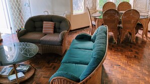 Un salón amplio con un sofá verde, un sillón de mimbre y un comedor.