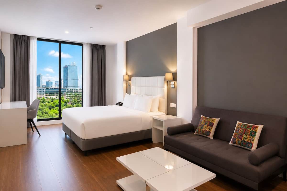 A modern hotel room with a large bed, a sofa, a desk, and a view of the cityscape.