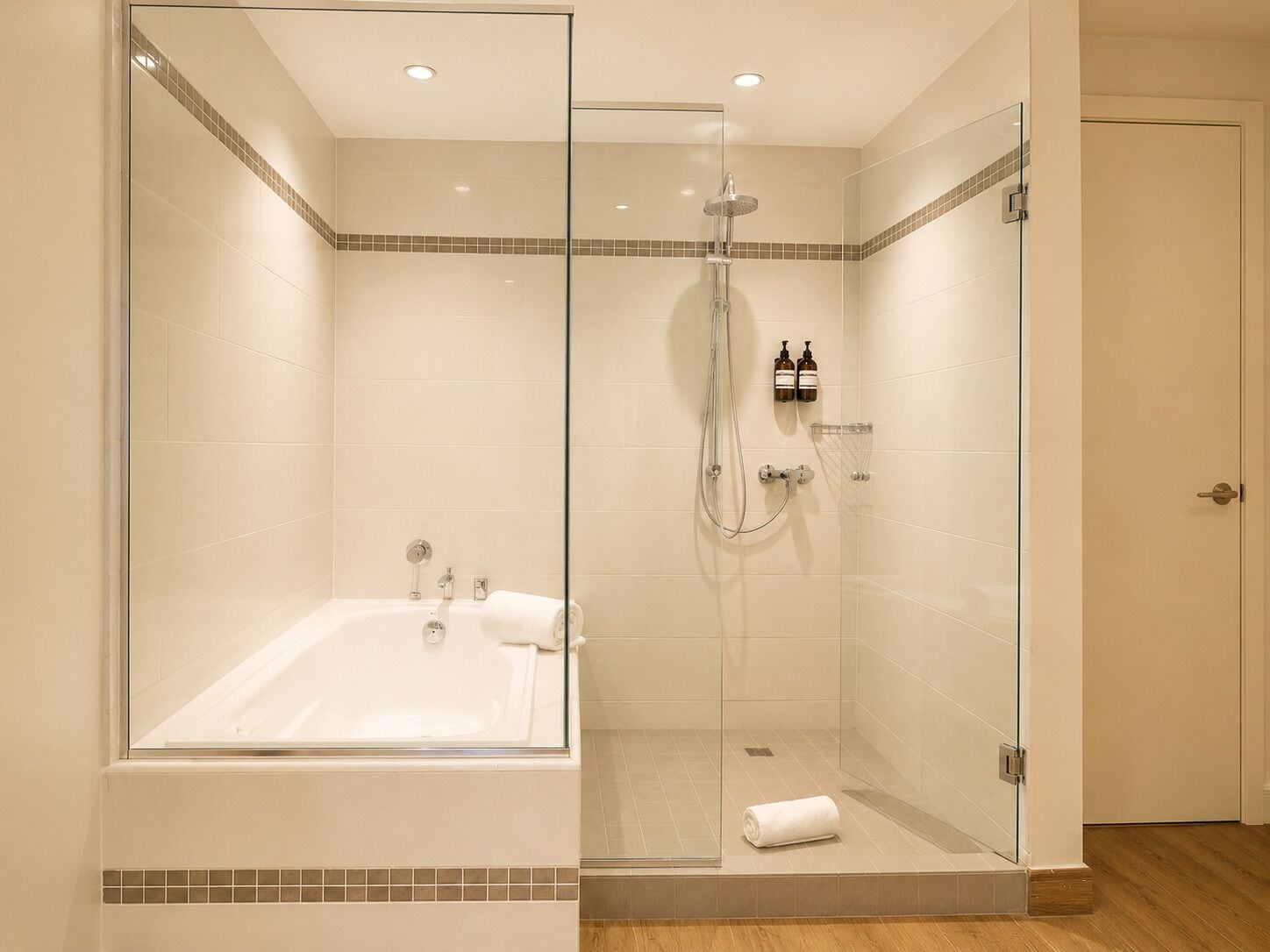 Un bagno moderno con doccia a vetro, una vasca freestanding e un'uscita verso un'altra stanza.