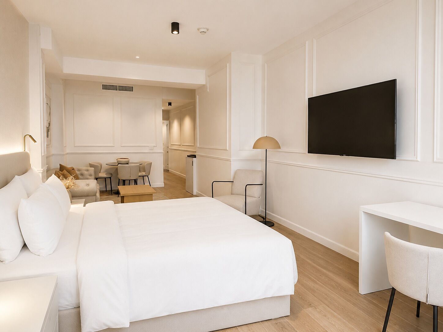 A modern hotel room with a large bed, a desk, a television, and a dining area.