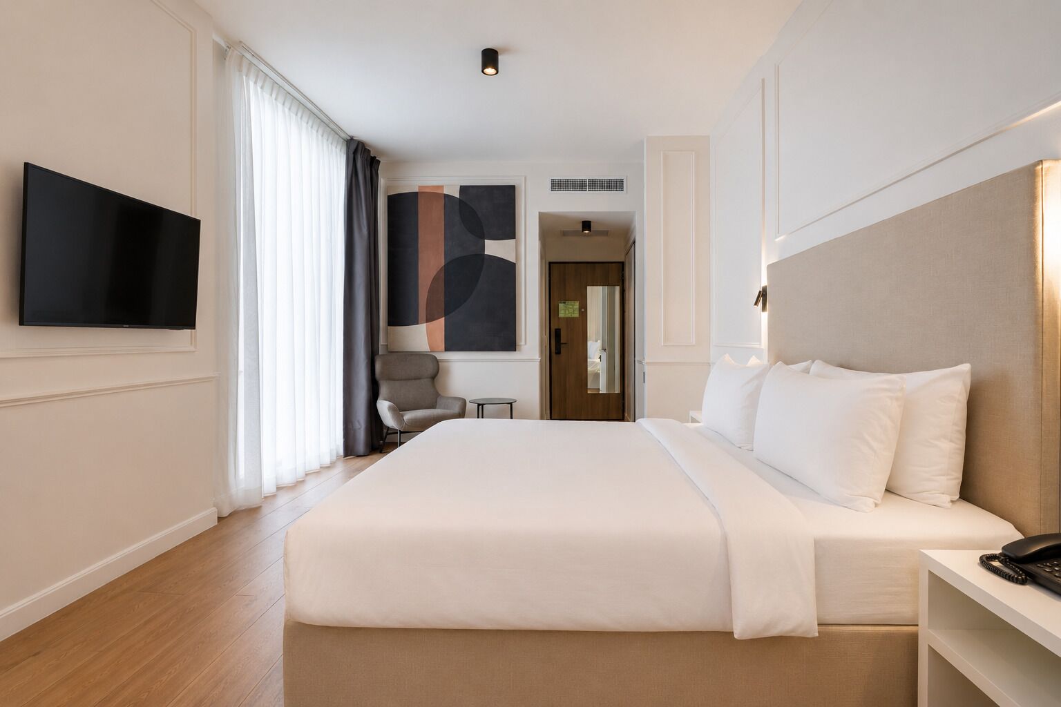 Ett hotellrum med en stor säng, en TV, en stol och ett skrivbord med en telefon.