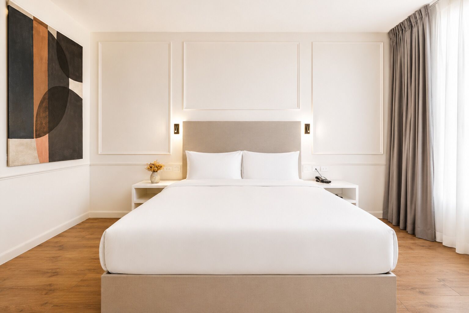 Una habitación de hotel moderna con una cama grande, una mesita de noche con una lámpara, un florero y un cuadro en la pared.