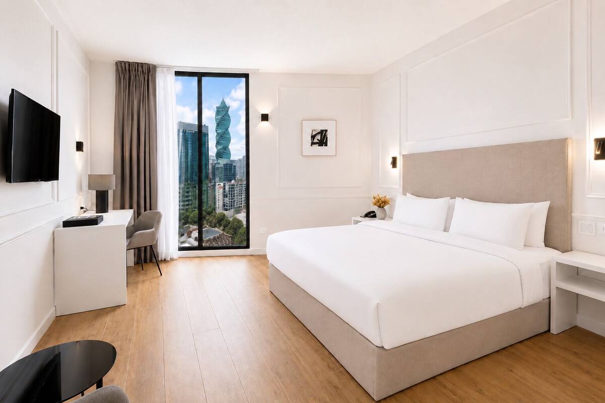 Une chambre d’hôtel moderne dotée d’un grand lit, d’un bureau, d’une chaise, d’une télévision et offrant une vue sur le paysage urbain.
