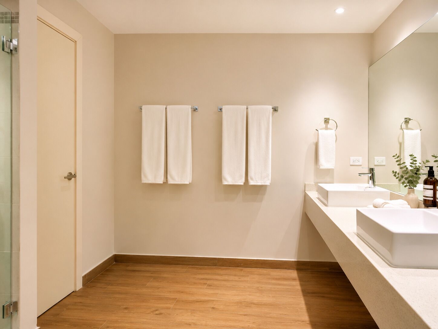 A modern bathroom with two sinks, a mirror, and three towels hanging on the wall.