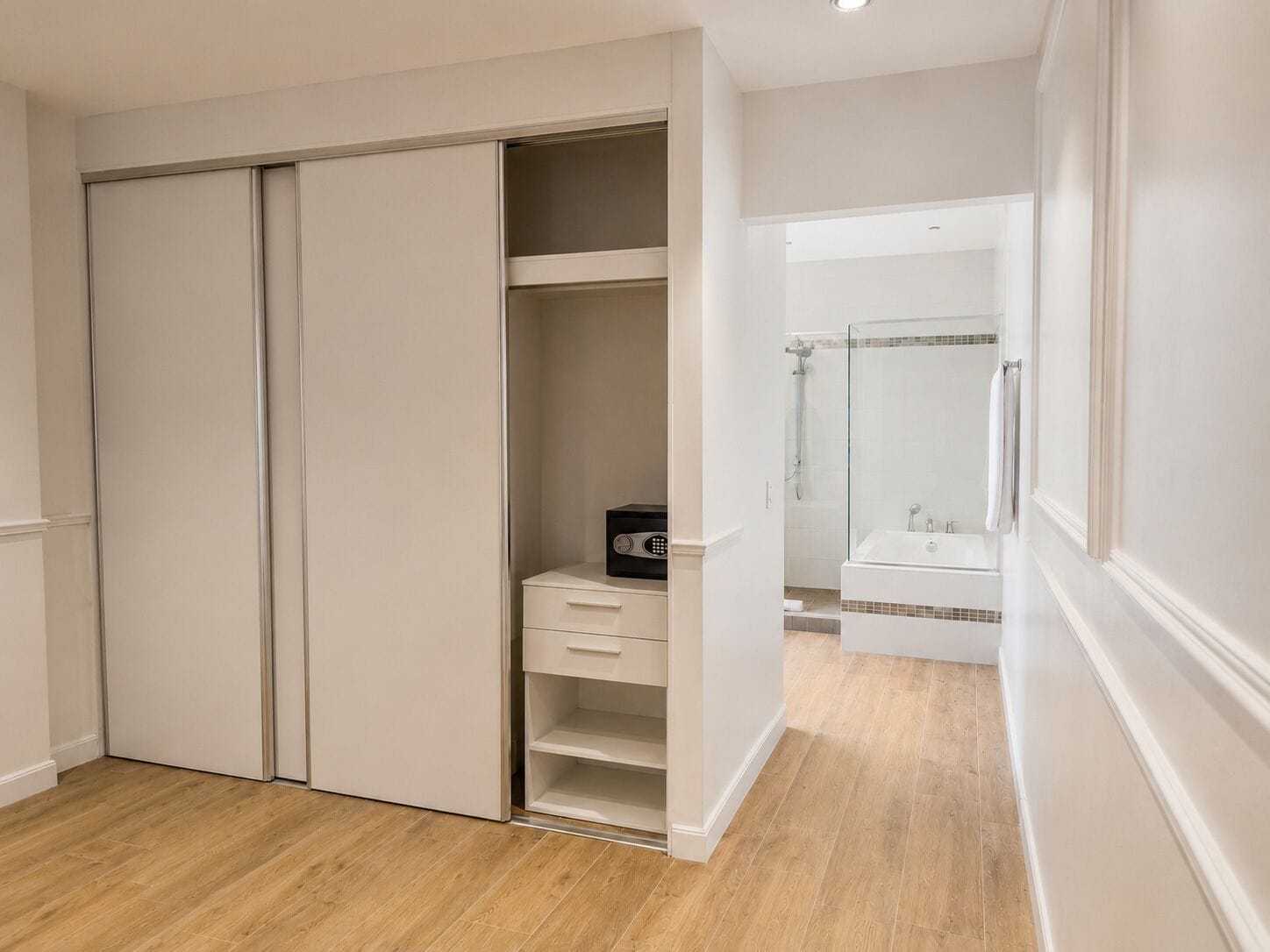 A walk-in closet with a built-in heater, a bathroom with a glass shower enclosure, and a wooden floor.