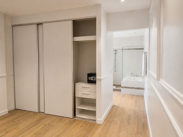 A walk-in closet with a built-in heater, a bathroom with a glass shower enclosure, and a wooden floor. - Hotel Mio Panama (Panama City)