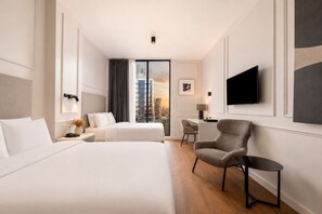 Een hotelkamer met twee bedden, een bureau, een stoel, een televisie en uitzicht over de stad.