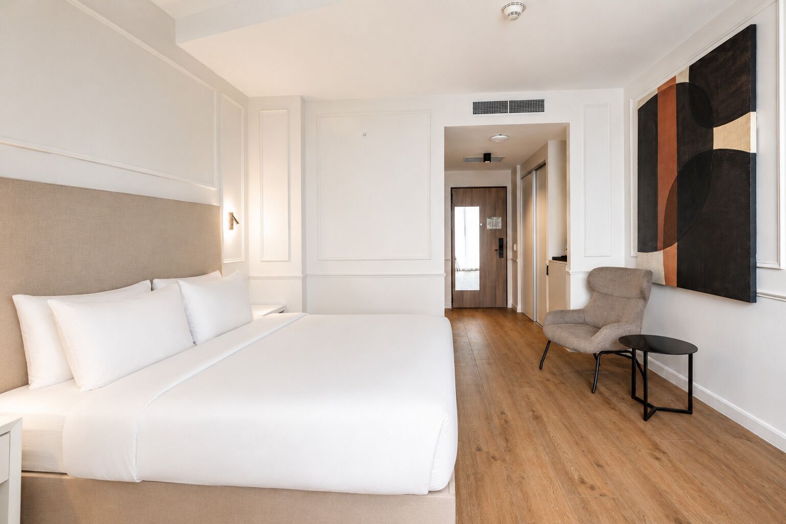 Una habitación de hotel moderna con una cama grande, una silla y un cuadro en la pared.