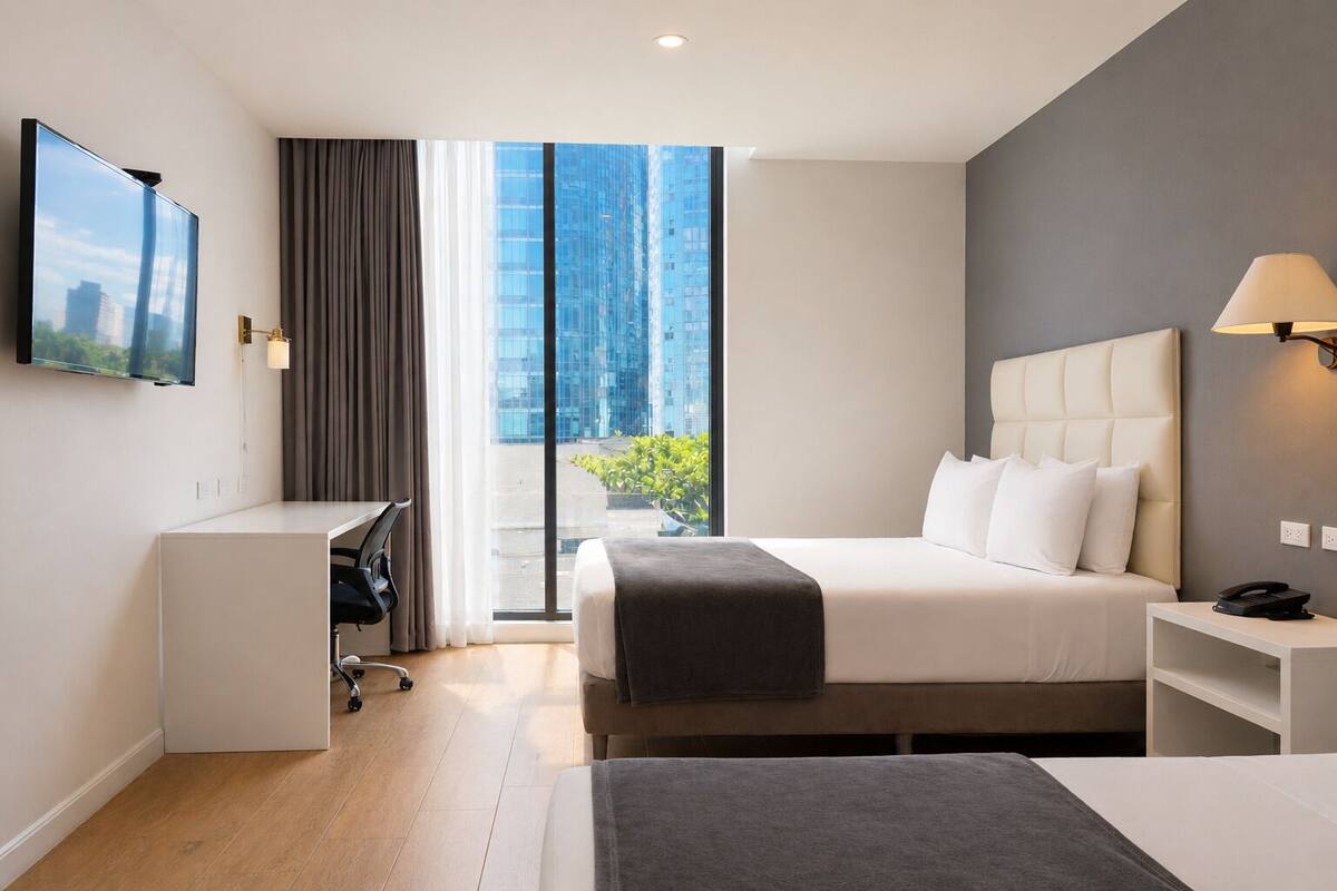 Une chambre d’hôtel moderne équipée d’un lit, d’un bureau et d’une grande fenêtre donnant sur la ville.