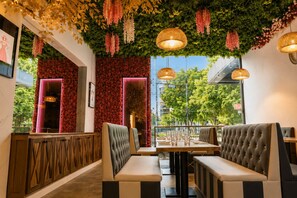 Un restaurant avec des banquettes, un mur rouge illuminé par des néons, des plantes suspendues et des luminaires suspendus.