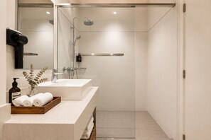 Een moderne badkamer met een douche met glazen wand, twee wastafels en een houten dienblad met handdoeken.