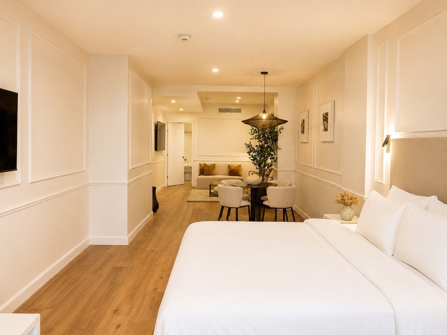 A hotel room with a large bed, a seating area with a table and chairs, a television, and a plant.