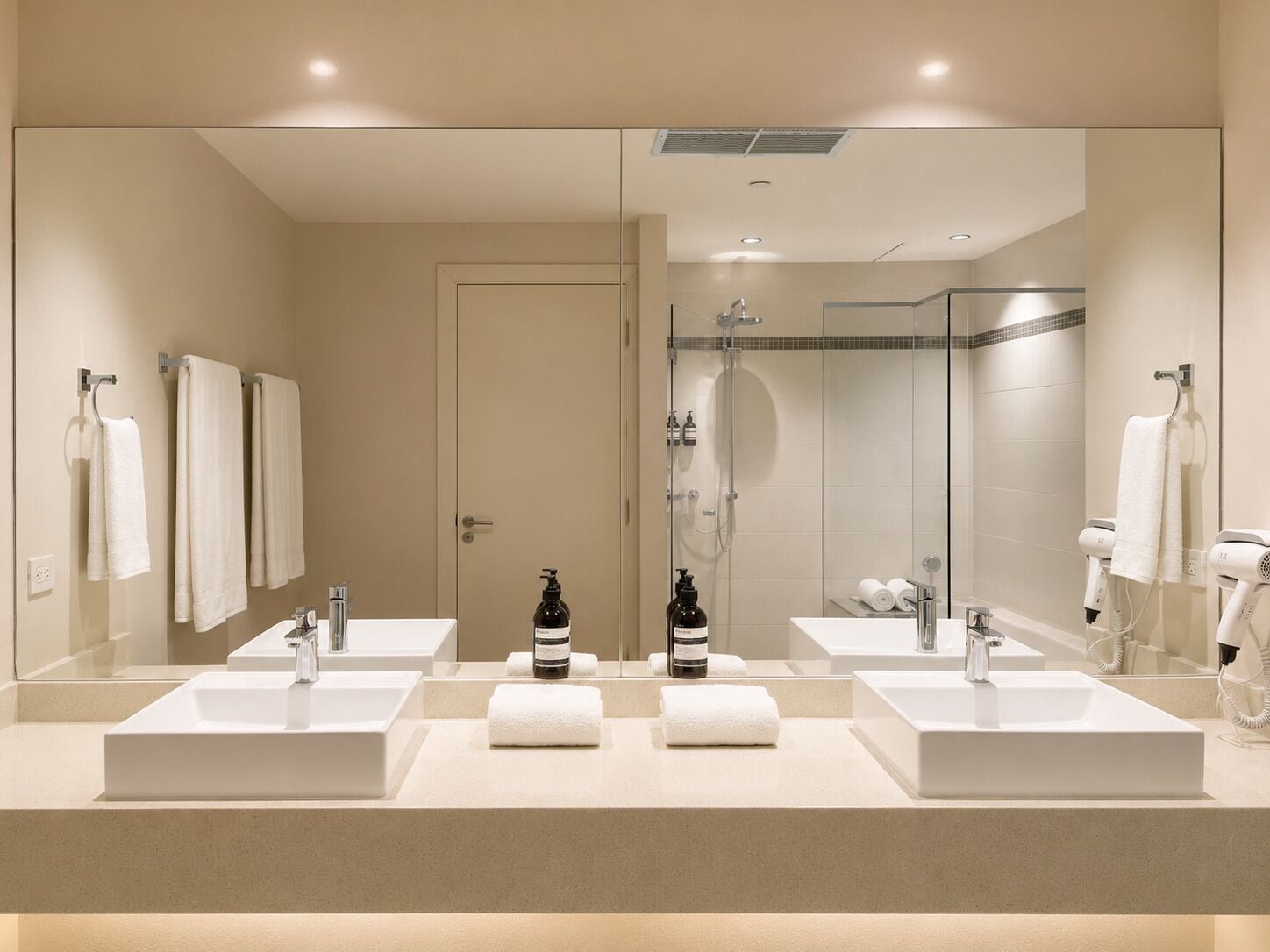 A modern bathroom with two sinks, a shower, and a large mirror.