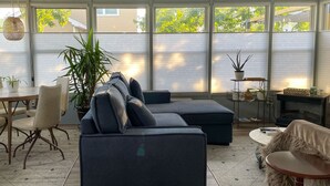 En moderne stue med en hjørnesofa, et spisebord med stole og et stort vindue med persienner.