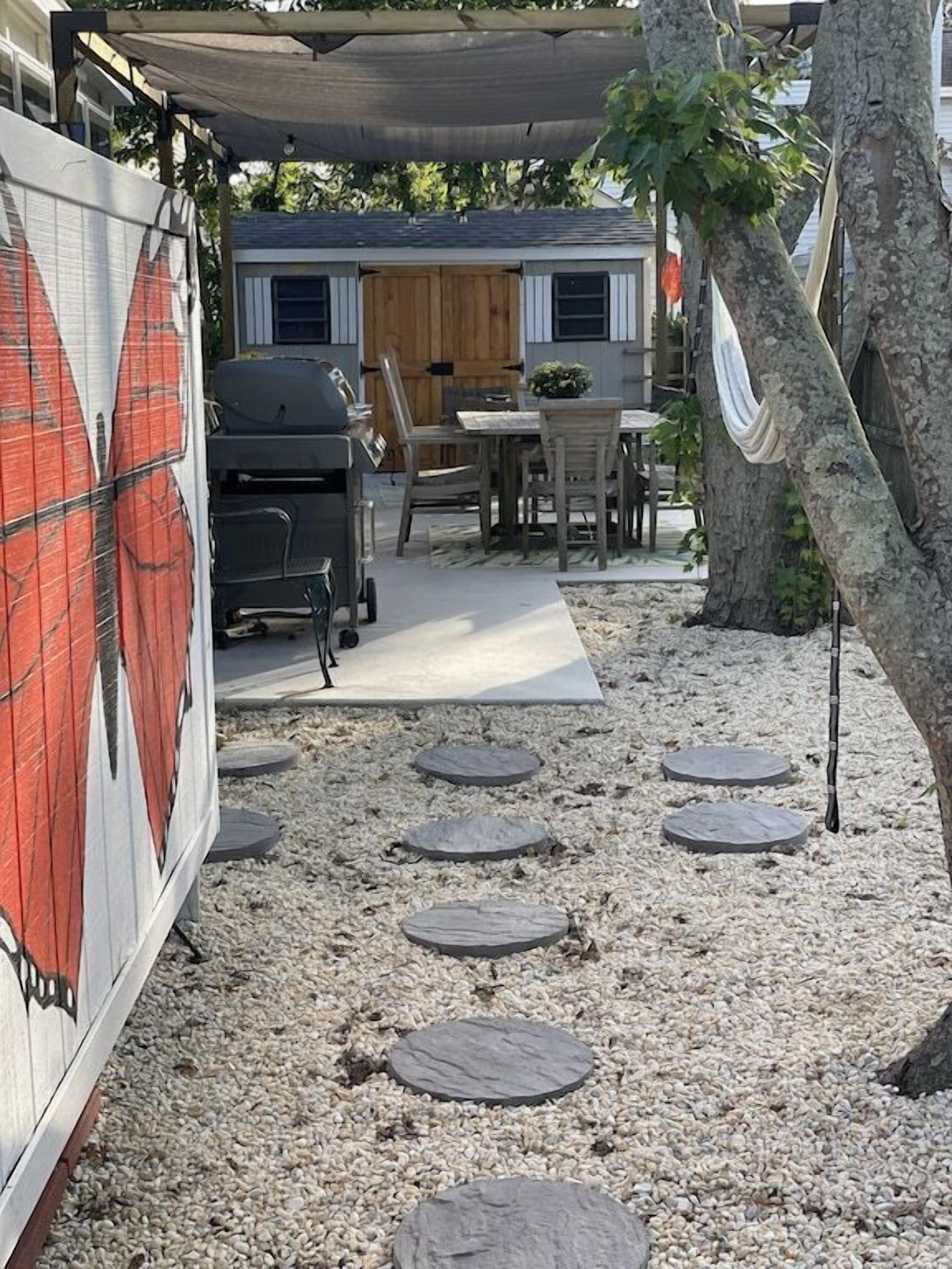 A covered outdoor patio area with a barbecue grill, a table with chairs, and a wooden door in the background.