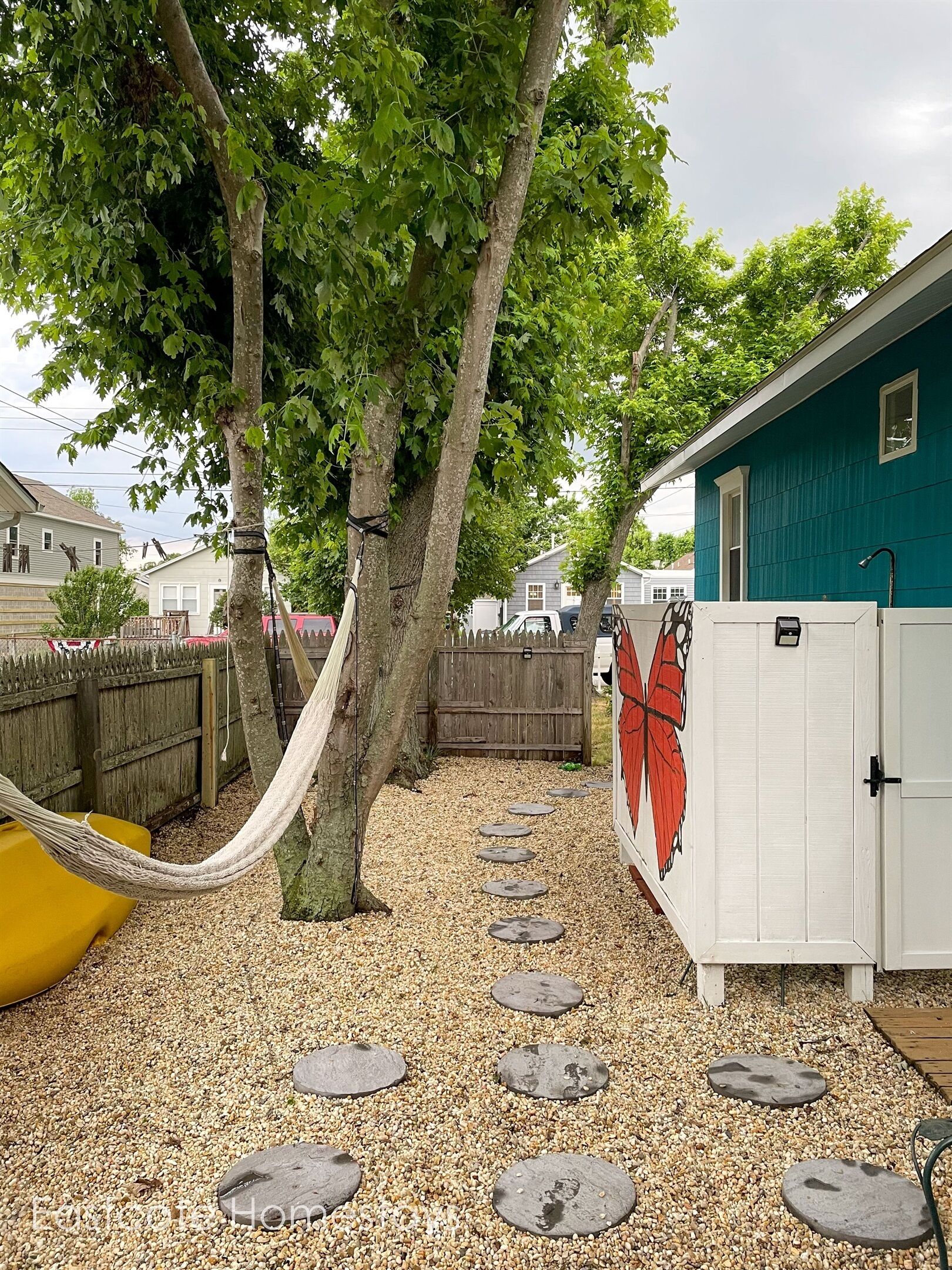 A backyard with a hammock, stepping stones, a wooden fence, and a butterfly mural on a shed.