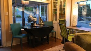 A dining area with a black table, two green chairs, a green office chair, and a window with a view of a street and greenery. - Cheerful 3 Bdrm w/ Kitchen & LR in West Seattle (Seattle)