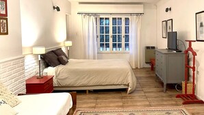 Un dormitorio con una cama, mesitas de noche, un aparador, un televisor y una ventana con cortinas.
