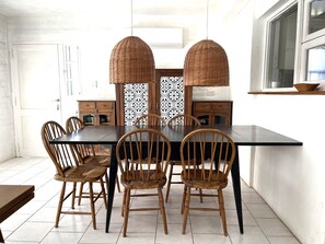 Un comedor con una mesa y sillas de madera oscura, dos lámparas de mimbre y un aparador con motivos decorativos.